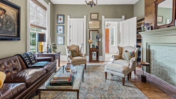 A living room with a brown leather sofa, a glass coffee table, and a patterned rug. There is a fireplace with a mirror above it.