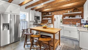 A modern kitchen with white cabinetry, a wooden dining table, and a brick accent wall.
