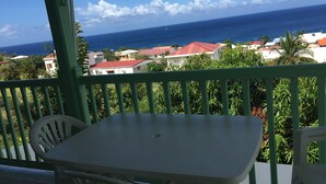 A balcony with a table and chairs, overlooking a coastal view with houses and the sea.