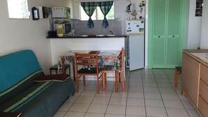 A compact living space with a sofa, dining table, chairs, a kitchenette, and a green door.