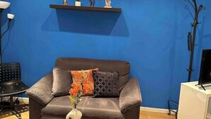 A living room with a blue wall, a brown leather sofa, a black coffee table with a vase, and two shelves with decorative items. - Piso, Apartamento, Centro de Madrid (Madrid)