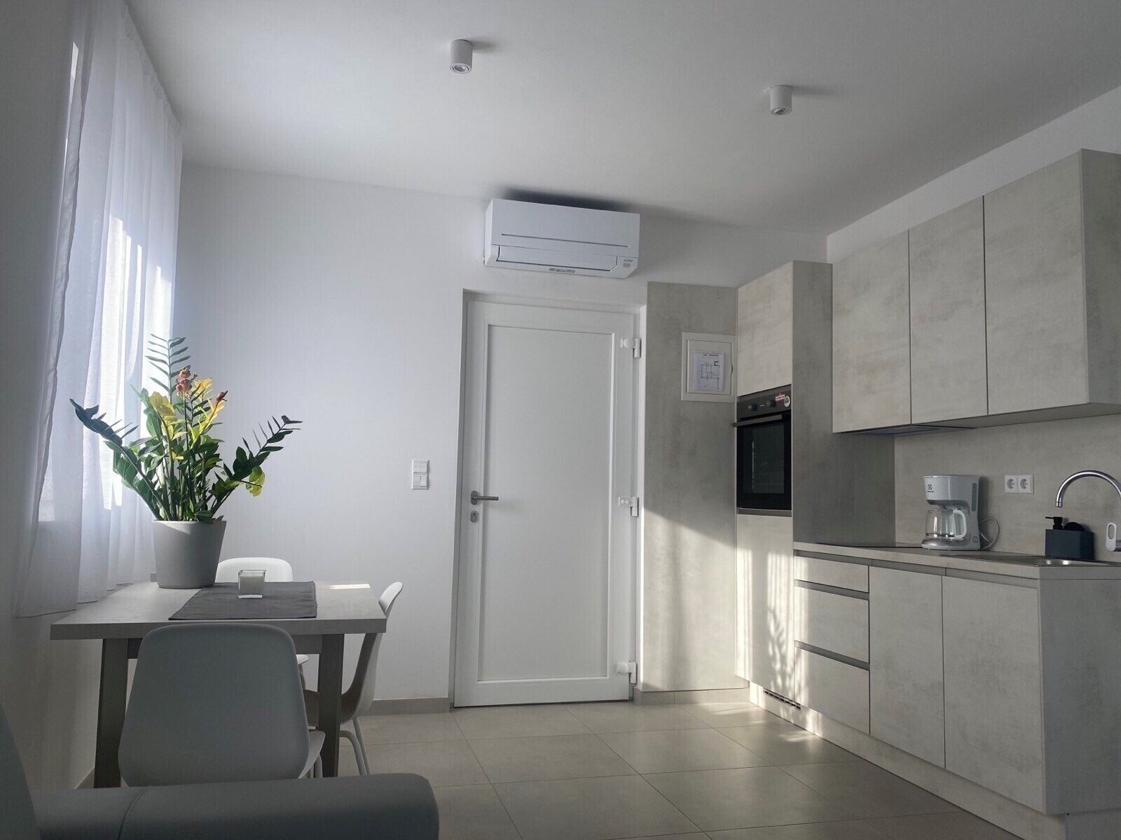 A modern kitchen with a built-in oven, a coffee maker, and a potted plant on the windowsill.