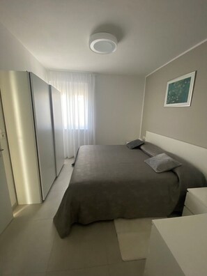 Ein modernes Schlafzimmer mit Bett, Nachttisch, Kleiderschrank und einem Fenster mit Vorhängen.