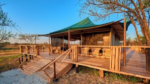 A wooden deck with a covered seating area and a staircase leading up to it. - Moyo Tented Camp (Serengeti)