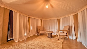 A room with a high ceiling, draped curtains, two wooden chairs, a woven table, and a hanging light fixture. - Moyo Tented Camp (Serengeti)