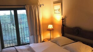 A hotel room with a large bed, a nightstand with a lamp, and a view through a window with curtains.