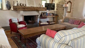 A cozy living room with a fireplace, red and beige sofas, a wooden coffee table, and a television.