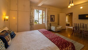 A bedroom with a large bed, a chair, a TV, and a dining area. - Mango Tree Courtyard Mussoorie (Dehradun)