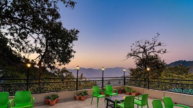 A terrace with green chairs and tables, potted plants, and a view of the mountains. - Mango Tree Courtyard Mussoorie (Dehradun)