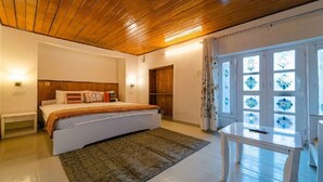 A bedroom with a wooden ceiling, a bed with a patterned bedspread, a bedside table, and a window with decorative glass panes. - Mango Tree Courtyard Mussoorie (Dehradun)