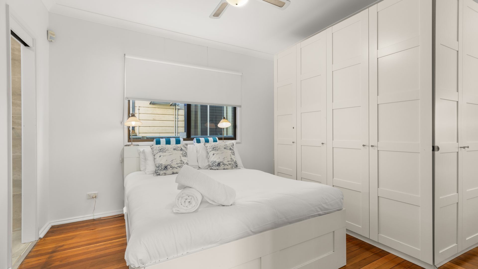 A bedroom with a bed, two bedside lamps, a window, and a wardrobe.