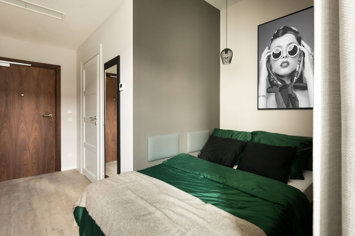 Ein Schlafzimmer mit einem Bett, einer Tür, einer Lampe und einem gerahmten Bild an der Wand.