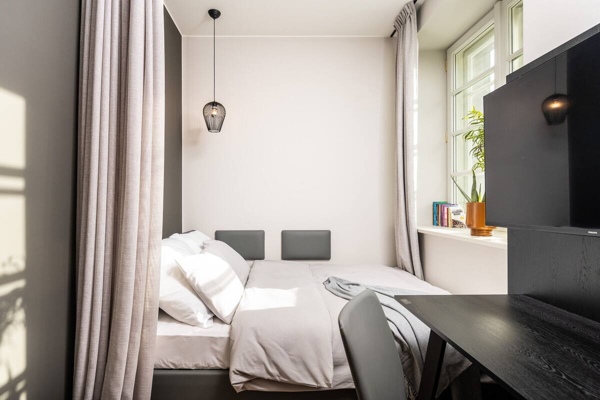 Ein Schlafzimmer mit einem Bett, einem Nachttisch und einem Fenster mit einer Pflanze.