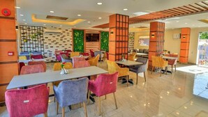 A modern restaurant with colorful chairs and tables, a brick wall with greenery, and a wooden ceiling. - The Palm Hotel Kafr El-Sheikh (Kafr el Shaikh)