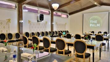 A conference room with multiple tables and chairs, a projector screen displaying "THE PALM", and a chandelier.