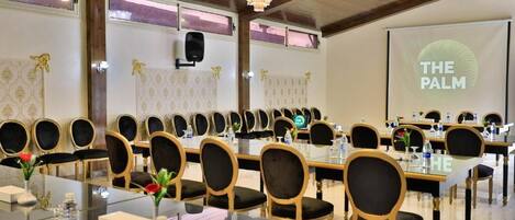 A conference room with multiple tables and chairs, a projector screen displaying "THE PALM", and a chandelier.