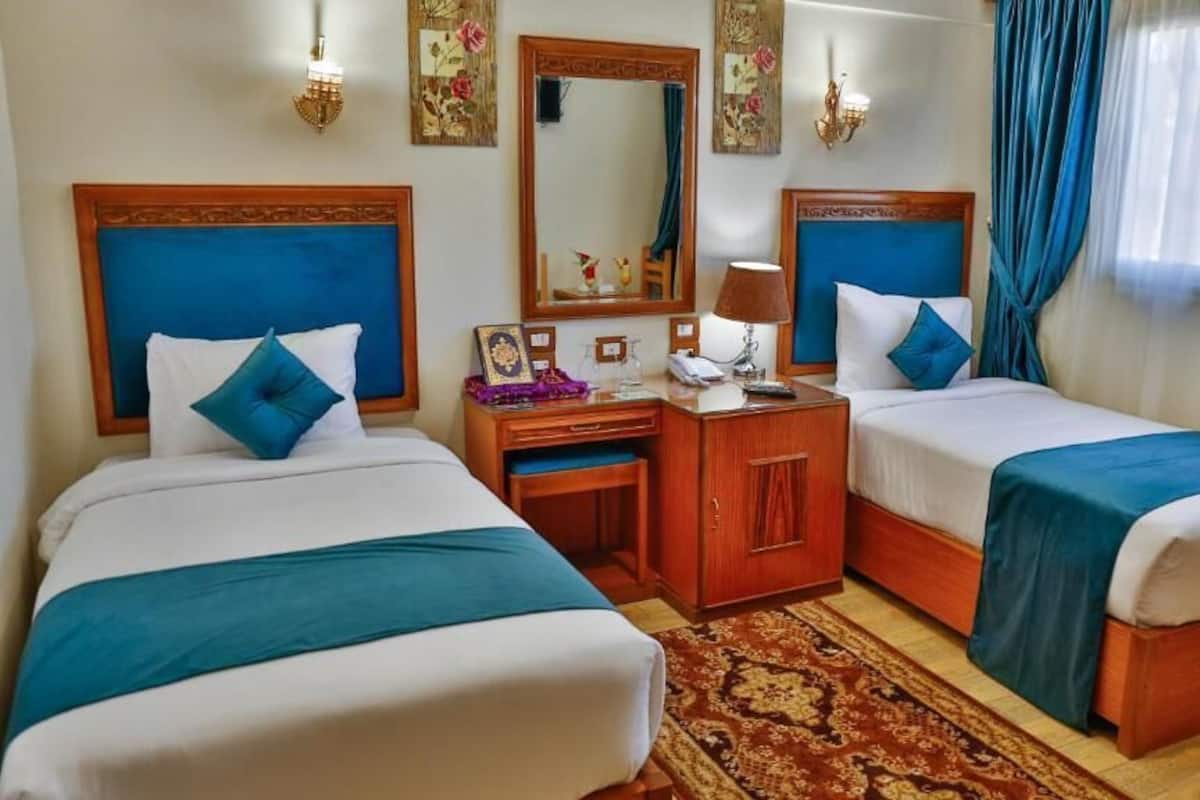 A hotel room with two beds, a wooden desk, a mirror, and a nightstand.
