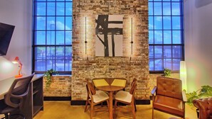 Una habitación con pared de ladrillo, un ventanal grande, una mesa con sillas y un televisor a la izquierda.