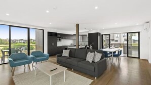 A modern living room with a grey sofa, two blue armchairs, a coffee table, and a large sliding glass door leading to a balcony.