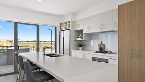 A modern kitchen with a large island, white cabinetry, and a view of the outdoors.