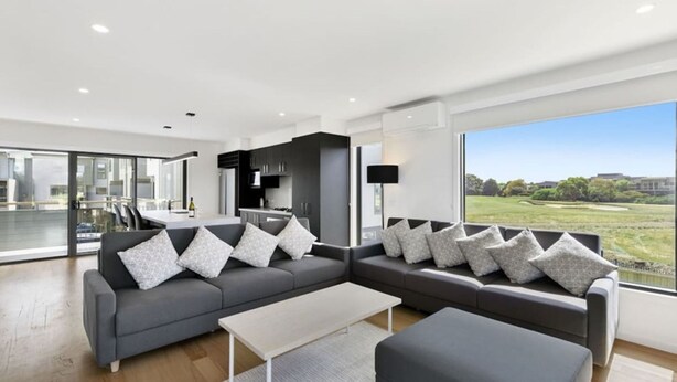 A modern living room with a grey sectional sofa, a coffee table, and a view of a golf course through large windows.