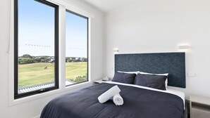 A modern hotel room with a large bed, a dark headboard, and a view of a green field through large windows.
