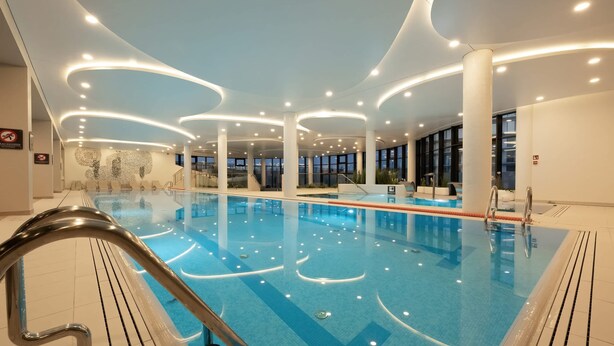 Una piscina interior de diseño moderno, con una fuente central y una zona junto a la piscina con barandilla de vidrio.
