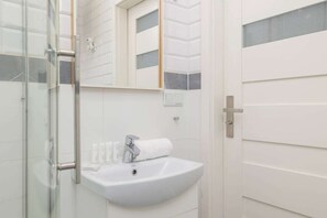 Ein modernes Badezimmer mit Duschkabine aus Glas, einem weißen Waschbecken mit Handtuch und einem Spiegel darüber.