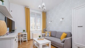 Una sala moderna con sofá, mesa de centro y televisor. Se ve una ventana con cortinas, un radiador y un armario.