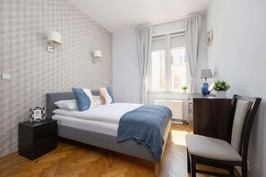 Ein Schlafzimmer mit Bett, Nachttisch, Sessel und einem Fenster mit Vorhängen.