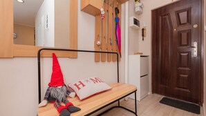 Un banco de madera con una decoración de gnomo y un cojín con la palabra 'HOME' en un pasillo con una puerta de madera y un espejo en la pared.