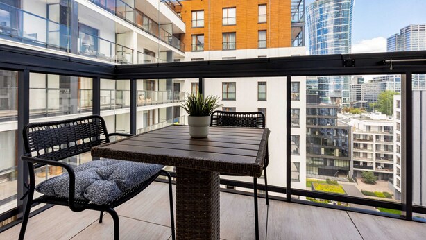 Un balcon avec une table et des chaises en osier, une plante en pot et une vue sur la ville.