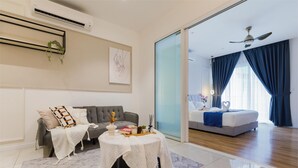 Een moderne hotelkamer met een grijze bank, een klein rond tafeltje met een witte tafelkleed en een bed met een blauwe sprei.