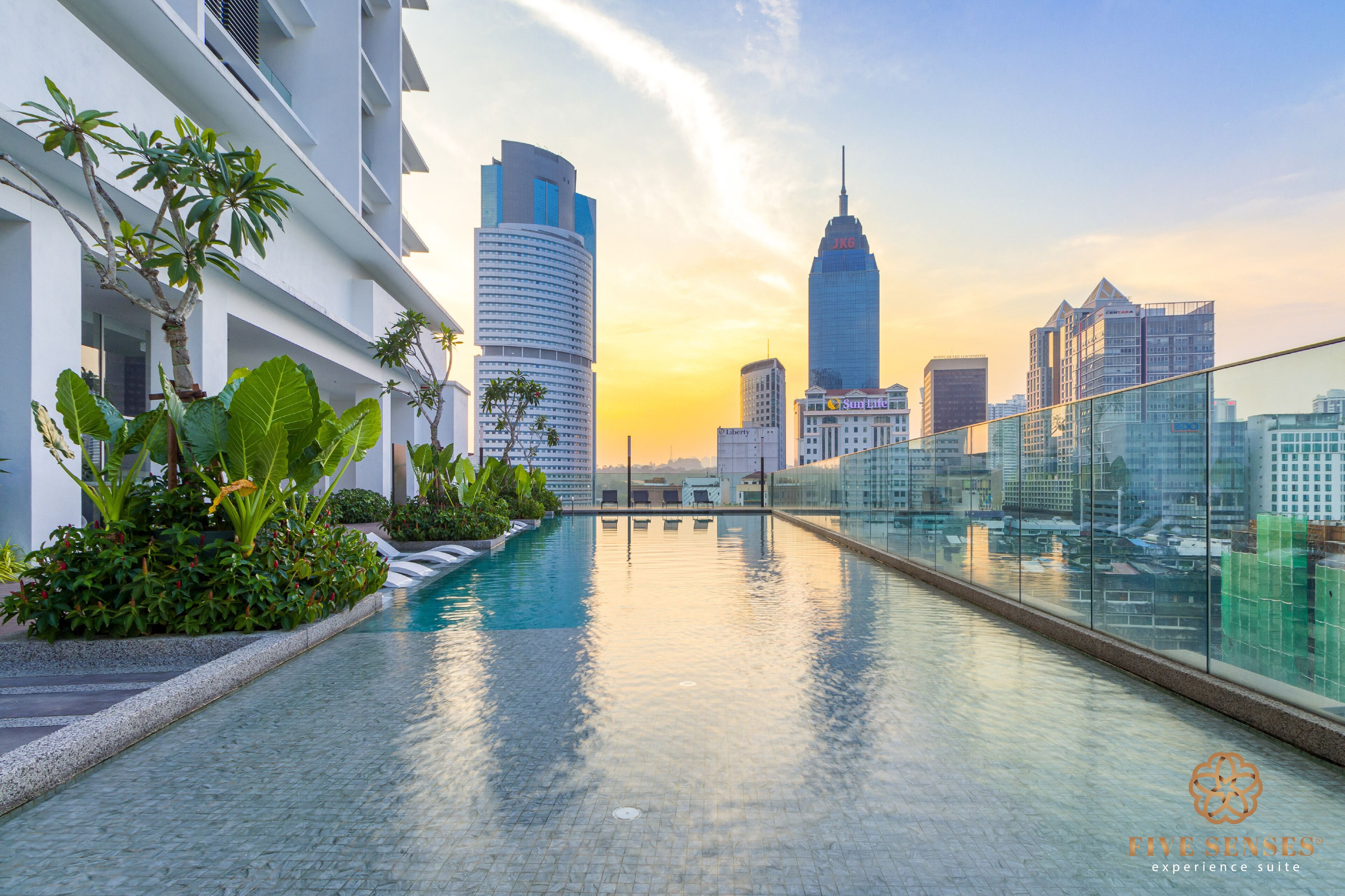Una piscina en la azotea con vistas al horizonte de la ciudad, edificios modernos y abundante vegetación.