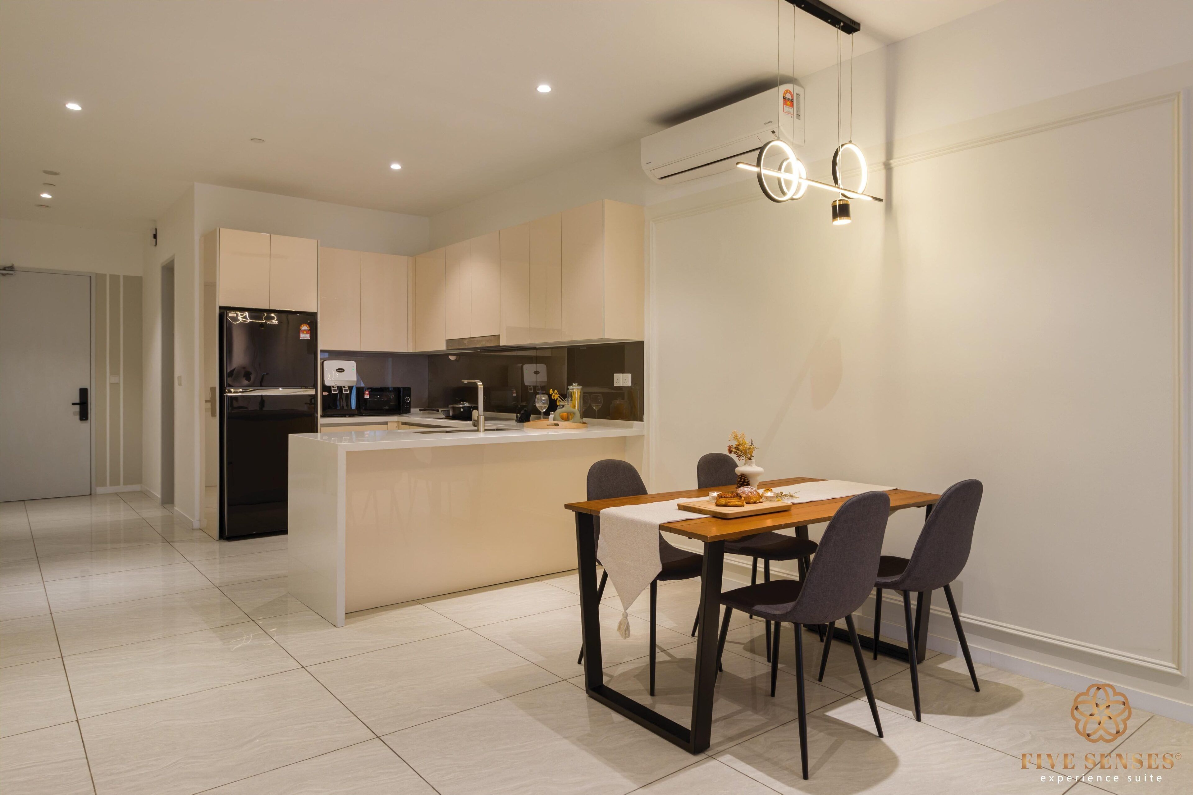 Une cuisine moderne avec un coin repas, comprenant un îlot central, des chaises foncées et un luminaire suspendu.