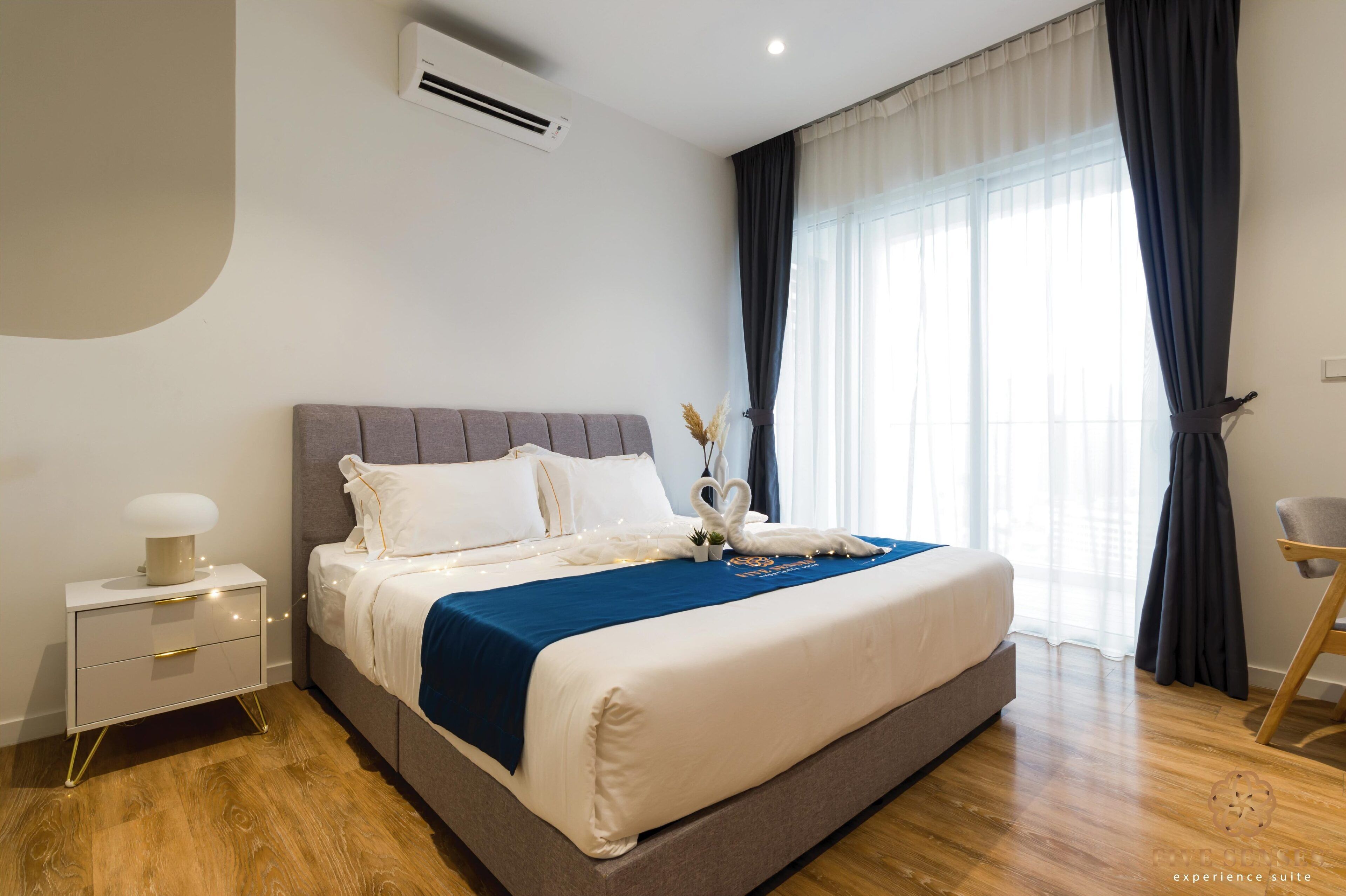 A modern hotel room with a large bed, a bedside table with a lamp, and a window with curtains.