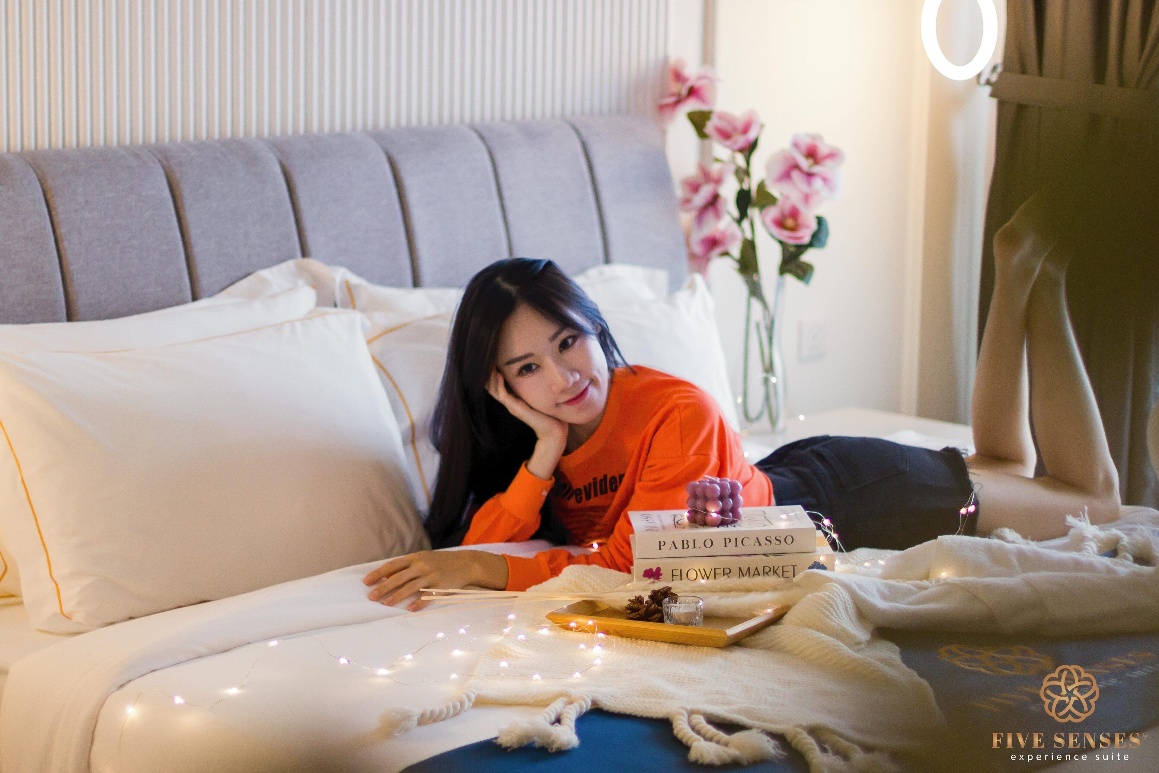 A person lying on a bed with a book titled "Pablo Picasso Flower Market" and a vase of flowers.