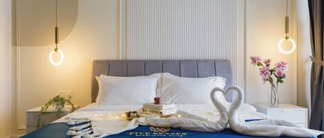 Un lit bien fait, recouvert d’une couverture bleue, agrémenté d’une pile de serviettes pliées en forme de cœur, d’une pile de livres et d’un vase rempli de fleurs roses.