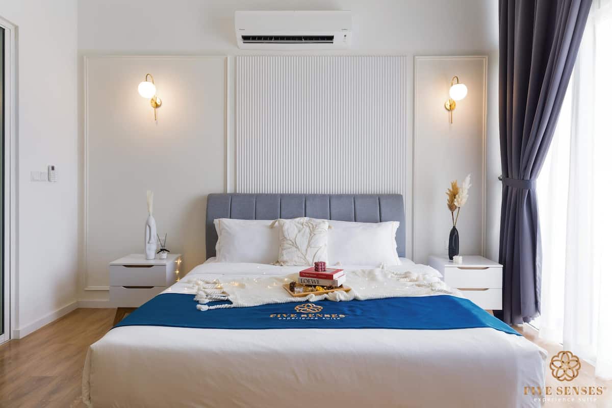 Een hotelkamer met een groot bed, twee nachtkastjes, een wandairconditioner en een raam met gordijnen.