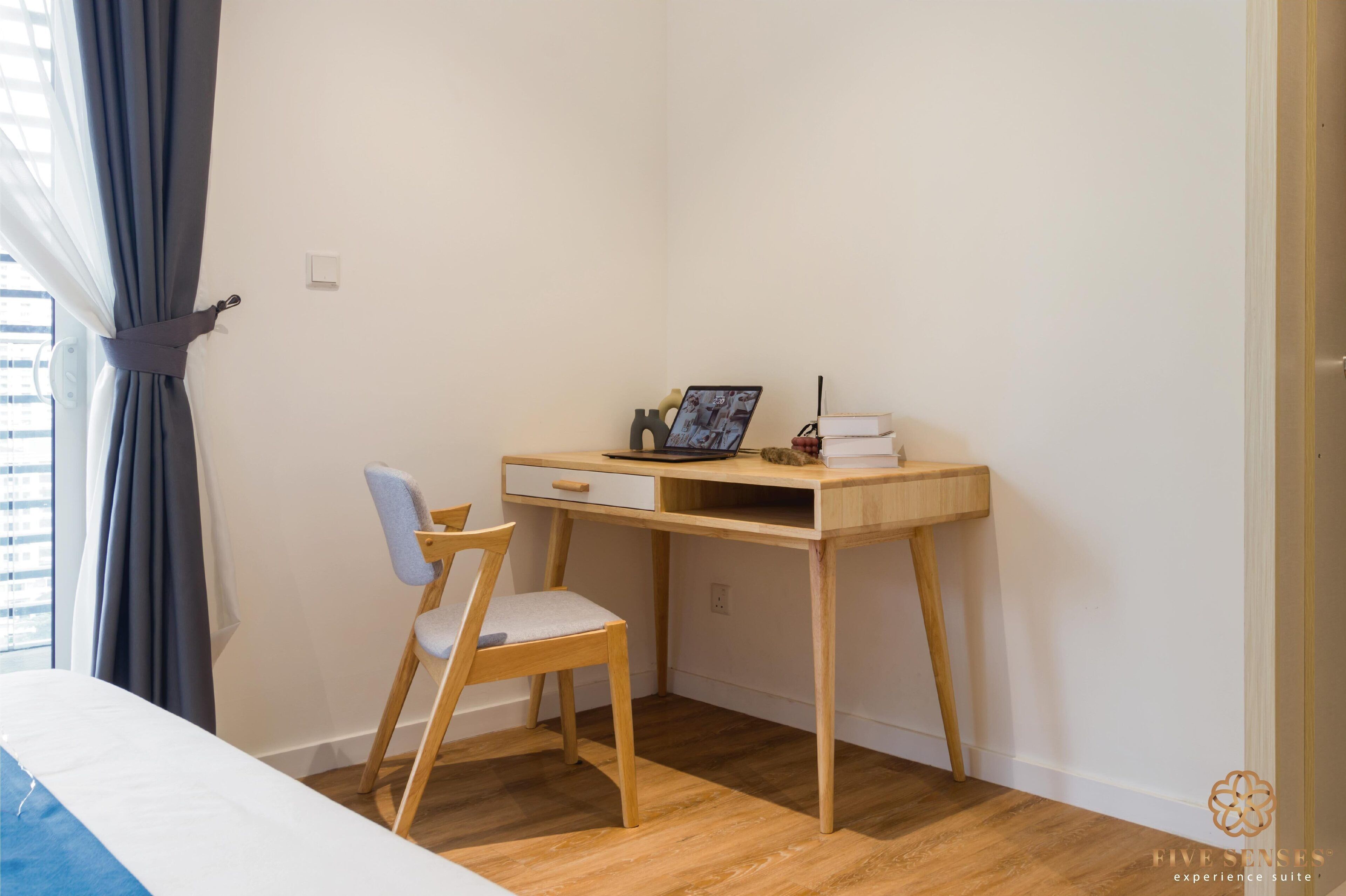 A room with a wooden desk, a chair, a bed, and a window with curtains.