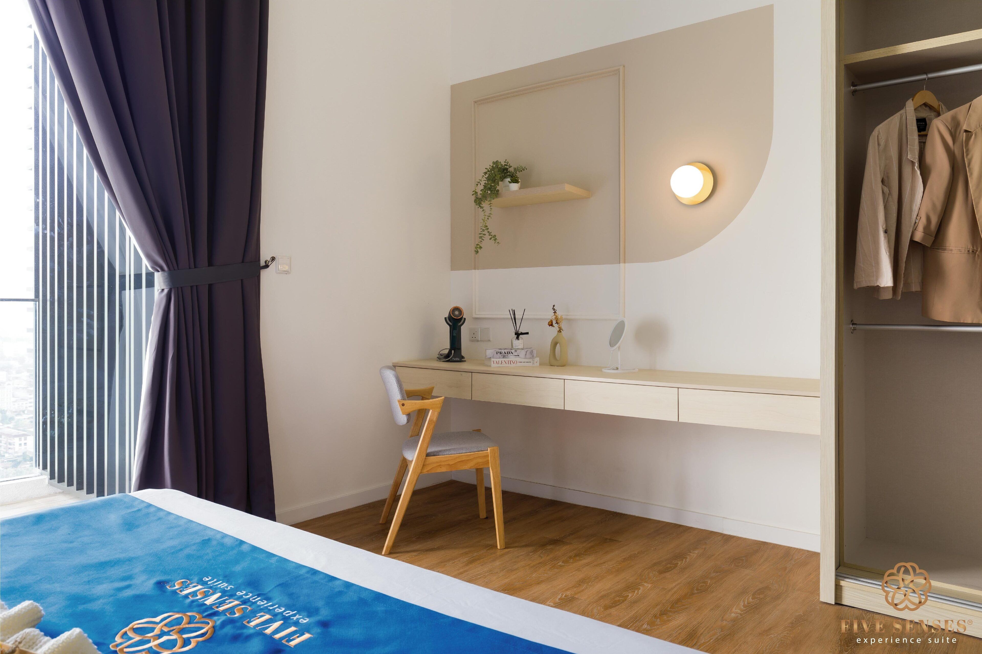 Ein Hotelzimmer mit Bett, Schreibtisch, Stuhl, Kleiderschrank, Spiegel, Ablage mit Pflanze und Nachttisch mit Lampe und Flasche.