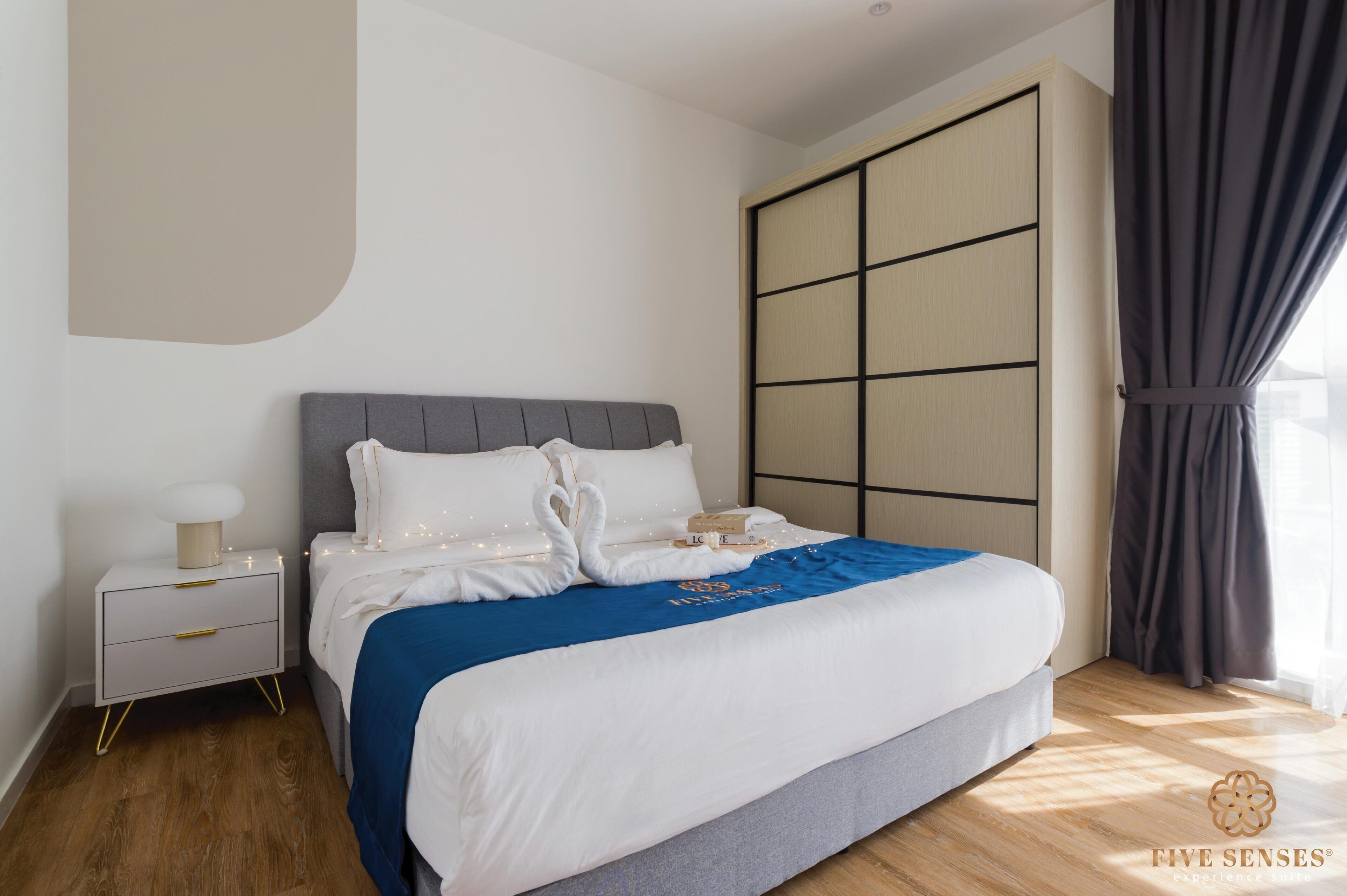 A neatly arranged bedroom with a bed, bedside table, and a large window with curtains.