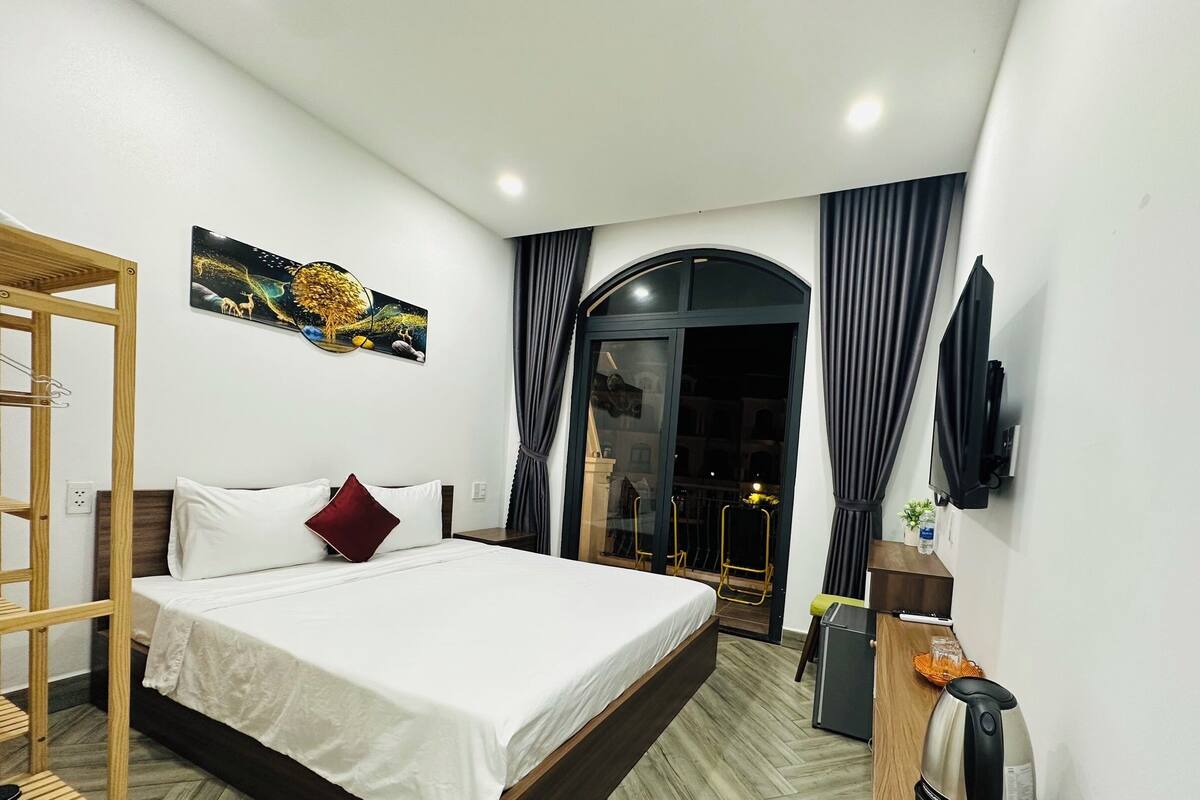Habitación de hotel moderna con cama, escalera de madera, un cuadro, televisor y vistas al exterior.