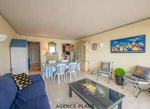 Una sala de estar con un sofá azul, una mesa de centro de vidrio y un comedor con mesa y sillas.