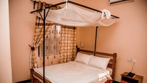 Una cama bien arreglada con dosel, una mesita de noche de madera con un teléfono y una ventana con cortinas.