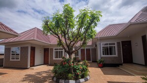 Un edificio residencial con fachada de ladrillo, un árbol central con flores rojas y un patio pavimentado.