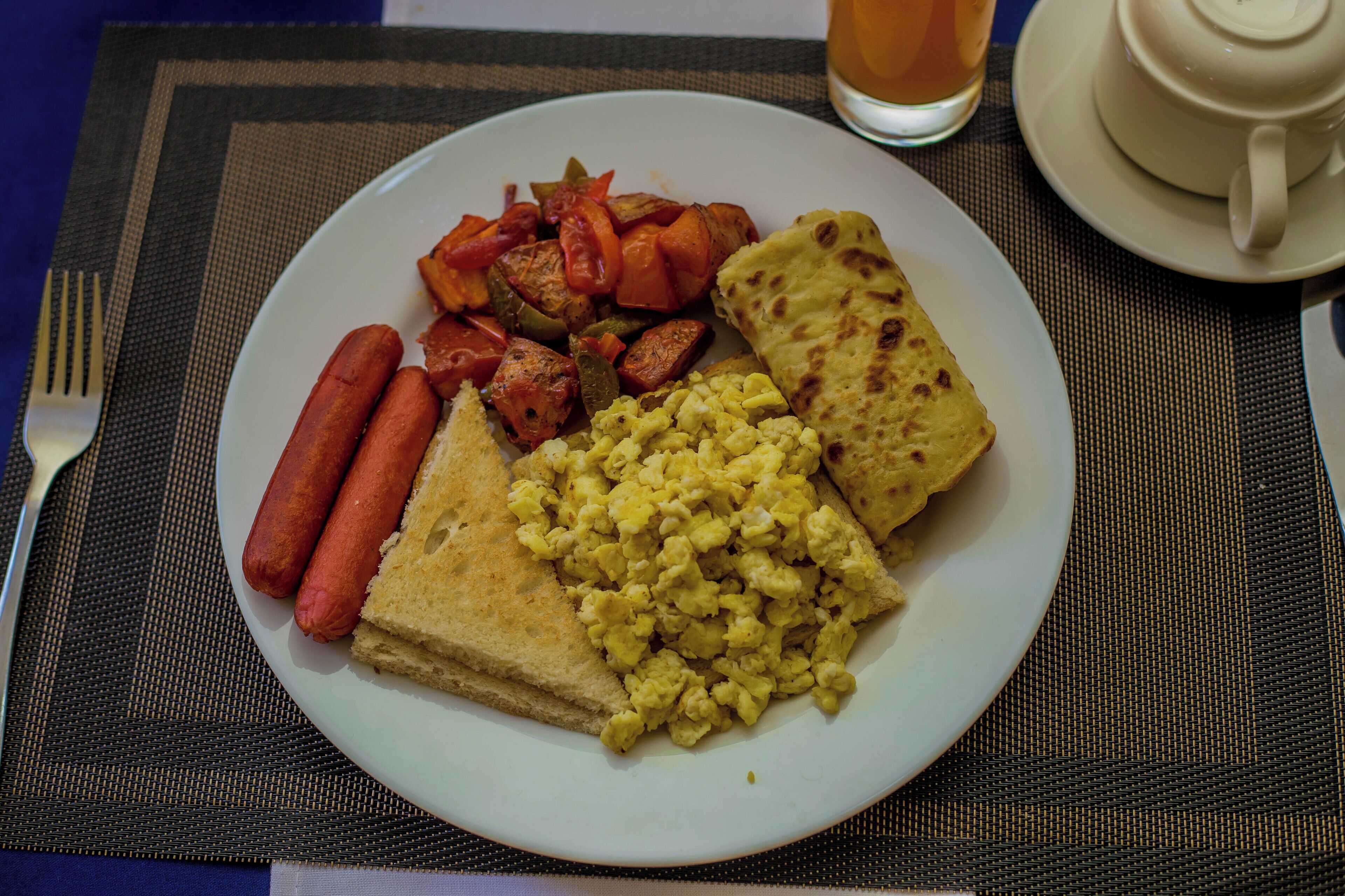 Een bord met hotdogs, roerei en een stuk platbrood op een placemat.