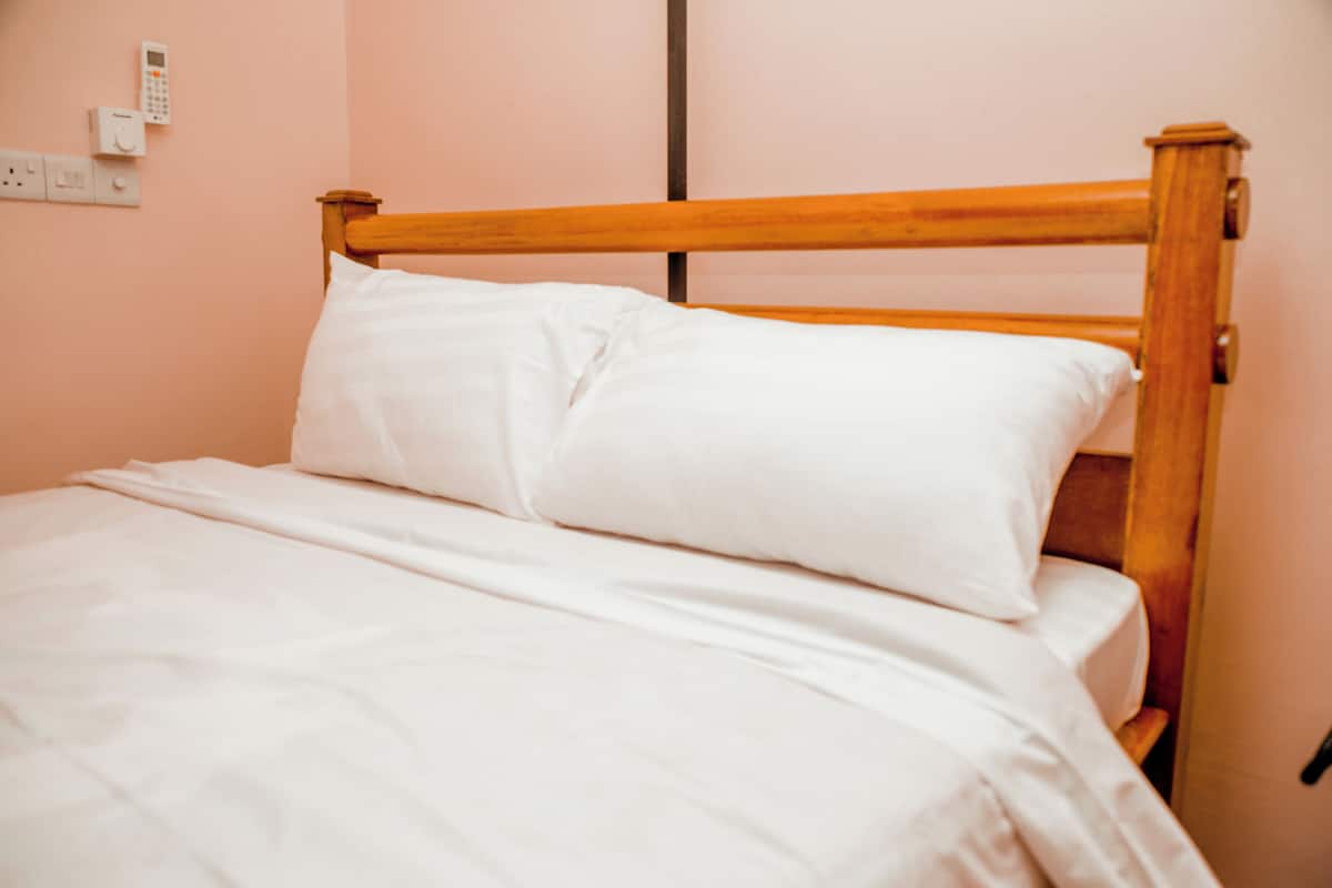 A single bed with white bedding in a room with pink walls and a wooden headboard.