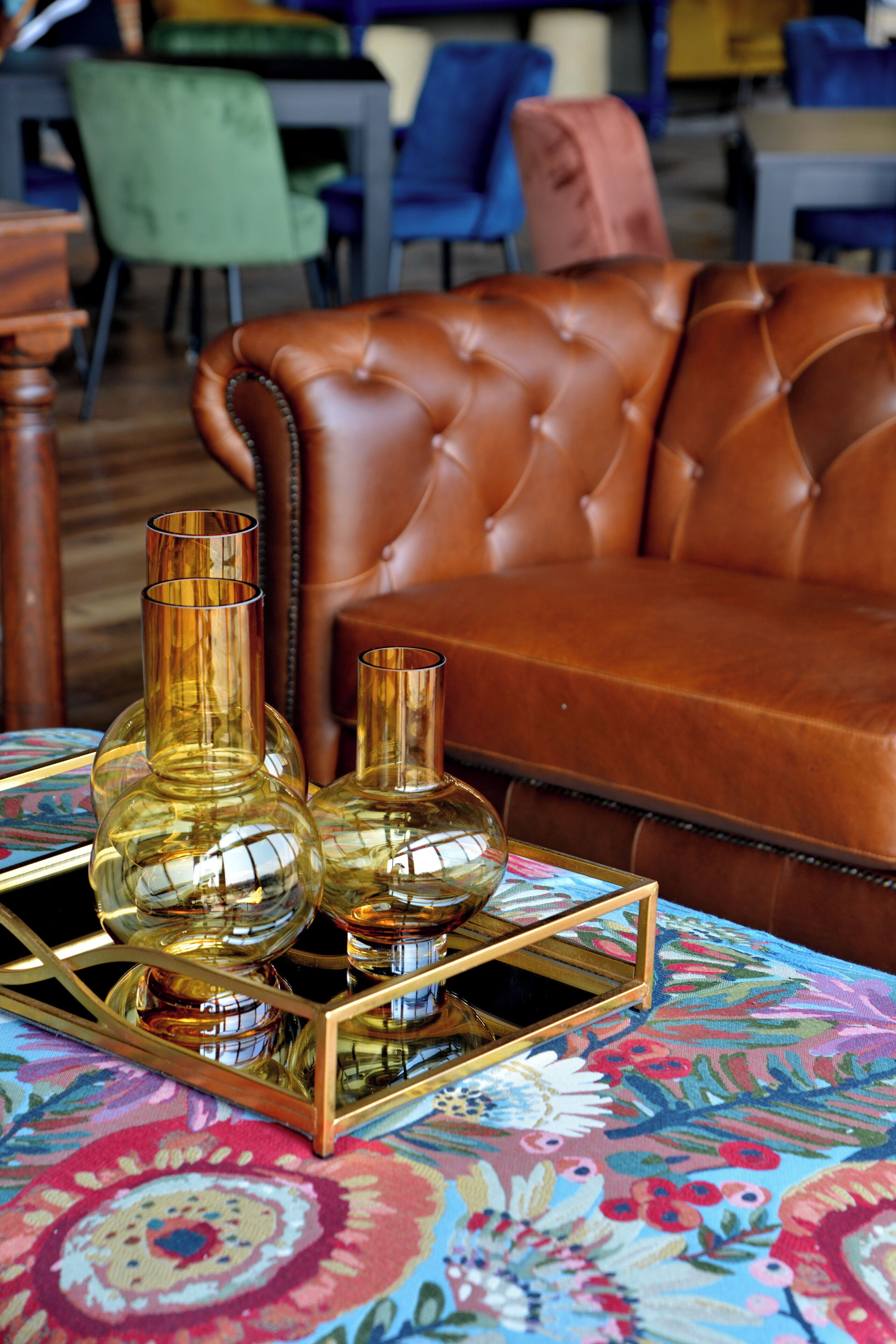 A brown leather sofa with a floral patterned tablecloth and two glass vases on a gold tray.