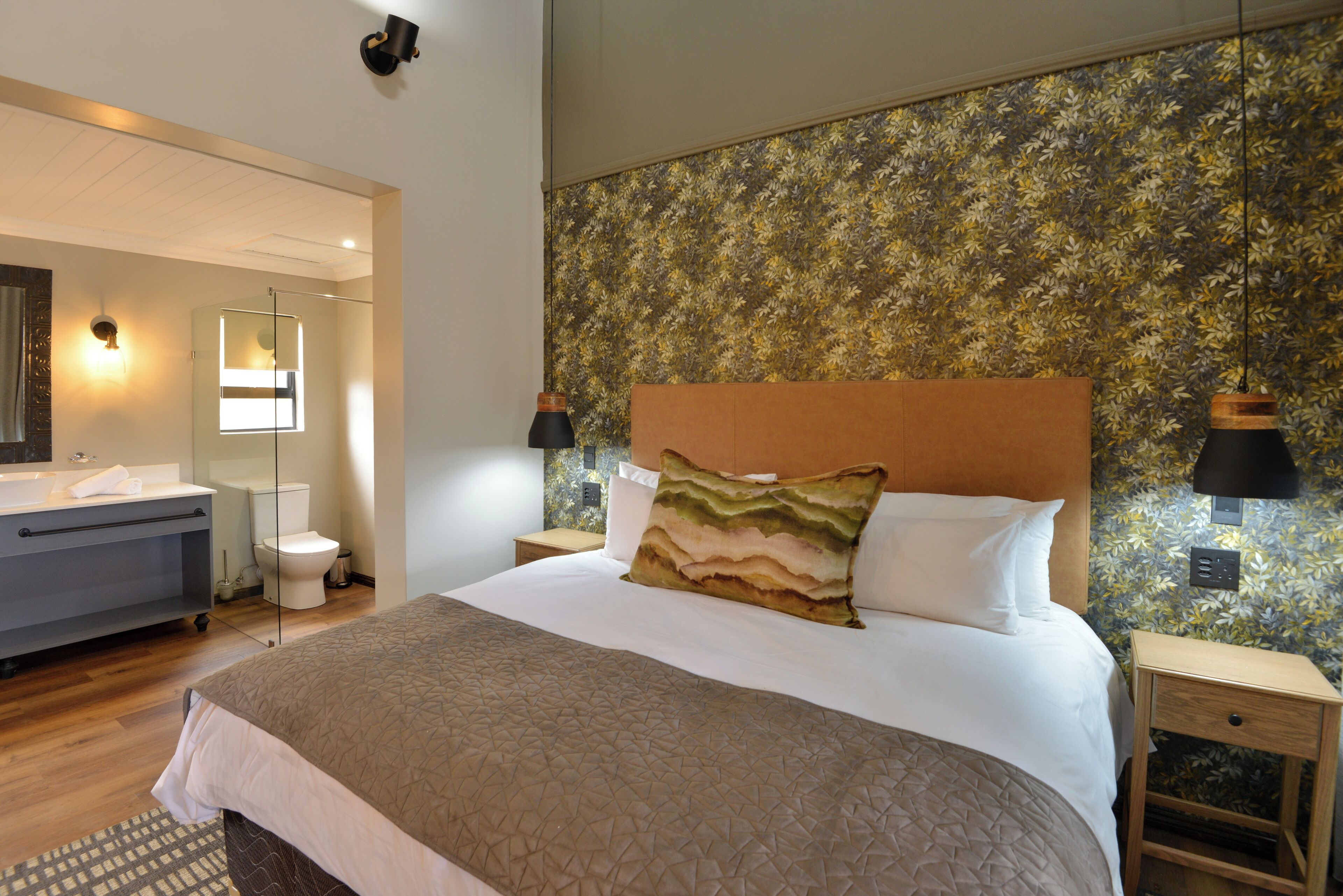 A hotel room with a large bed, a bathroom with a toilet and sink, and a wooden floor.